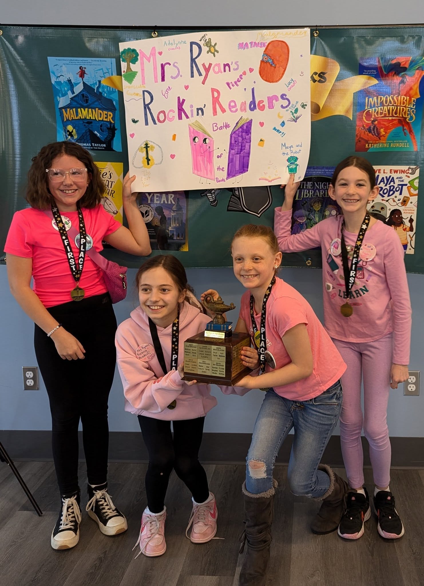 for young students stand together holding a trophy and a poster