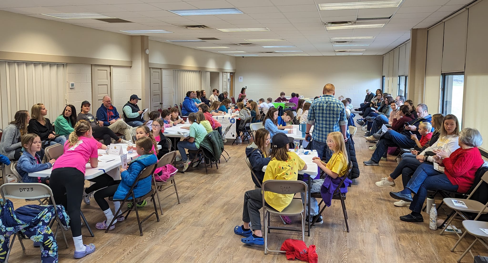 large room of students seated at round tables participating in the library's Battle of the Books event