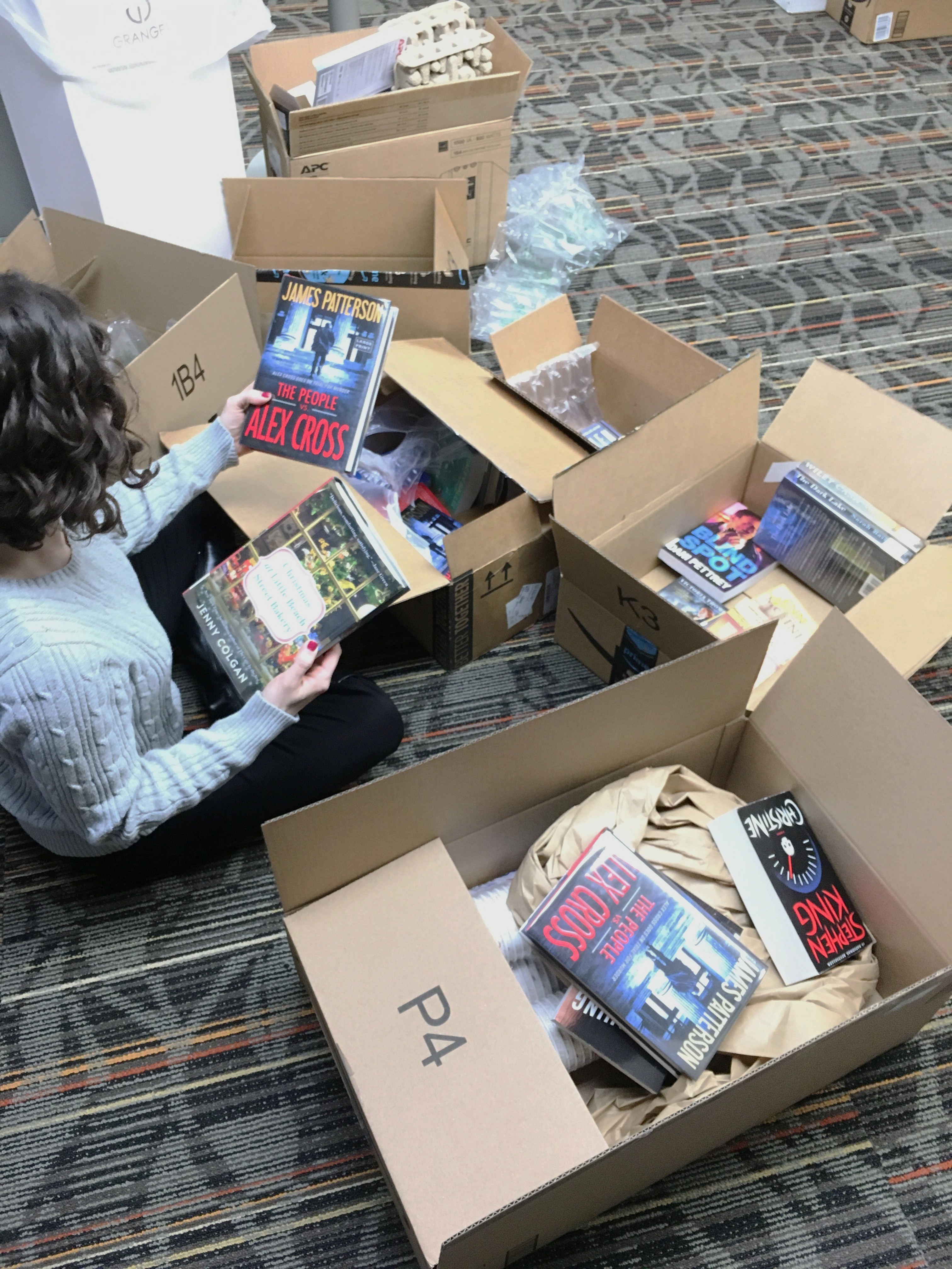 a person sits on the floor of the library surrounded by boxes of books
