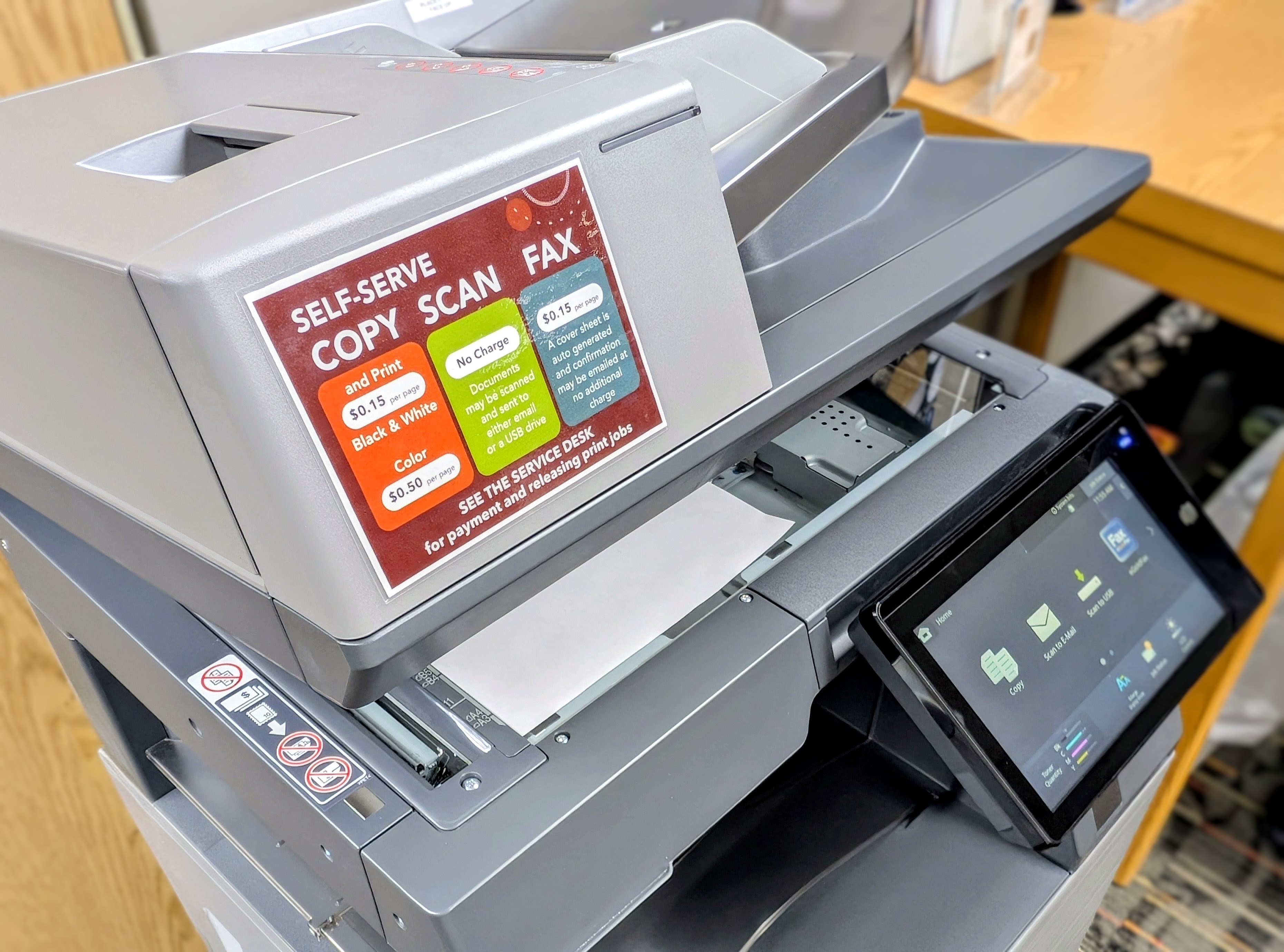 a close-up image of the top portion of the library copy machine, showing the display panel, copy bed, and a sign that lists service pricing