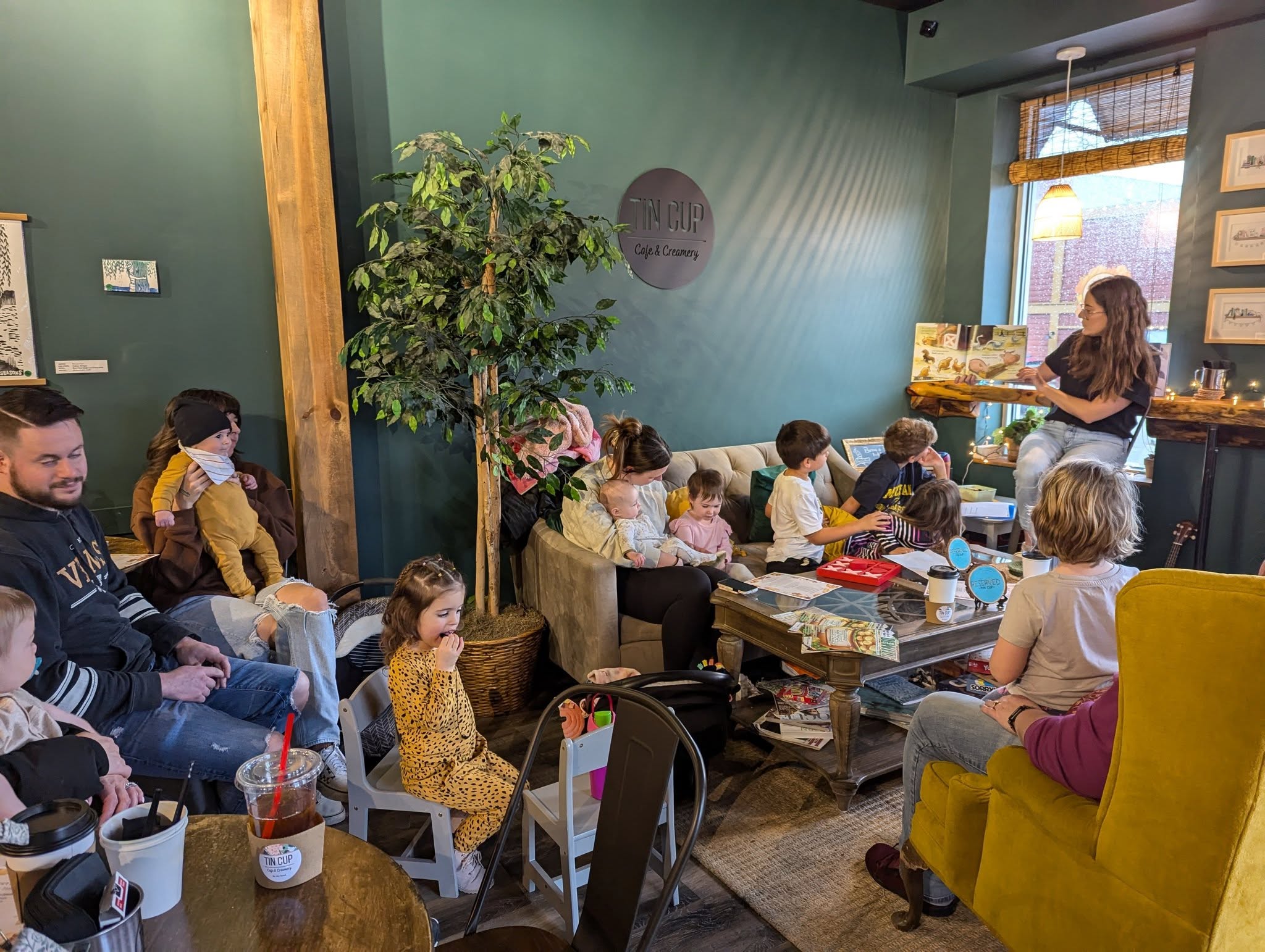 families with young children are seated around a librarian reading a picture book at Tin Cup cafe