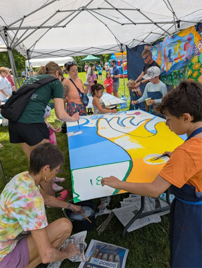 Group of people under a tent while painting a large canvas together.