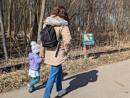 An adult and a child walking along a payment trail with a trail sign on the left hand side.