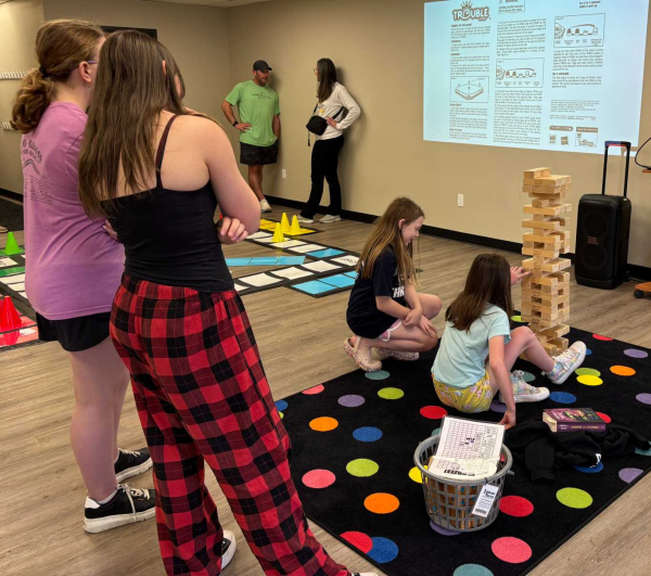 two teens look on as two girls play Giant Jenga