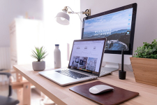 Laptop and monitor on a wooden desk with an aesthetic office in the background.
