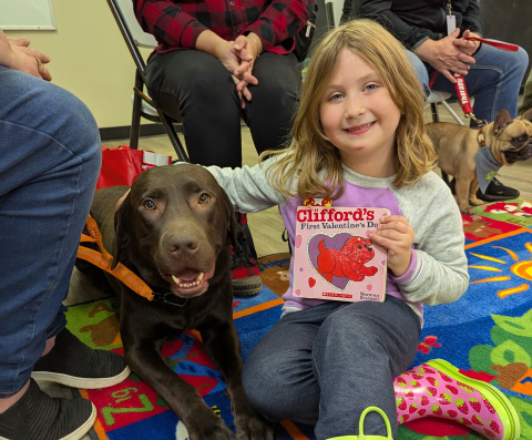 a girl holding a book next to a dog