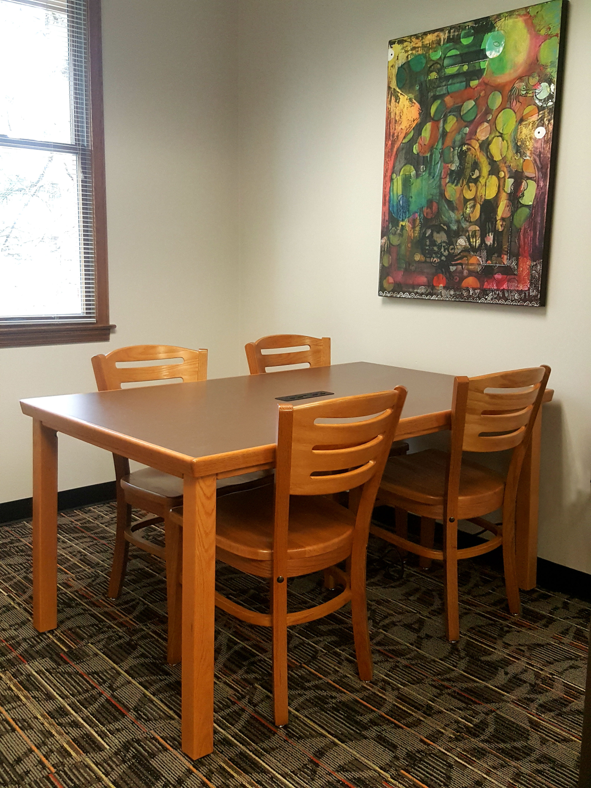 room with table that seats 4 people, a large artwork is hung on the wall and a window visible